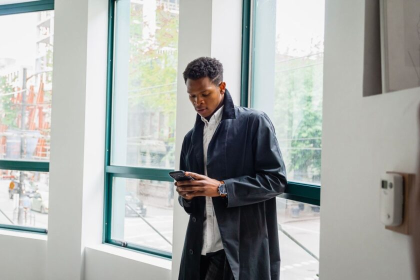 Mann ser på mobilen innendørs ved store vinduer
