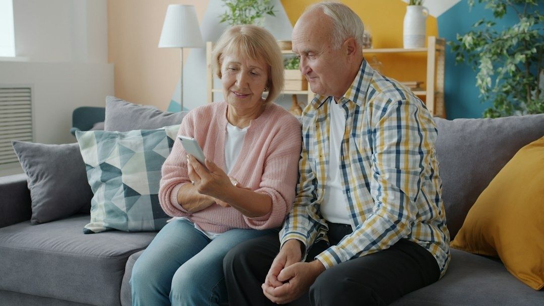 Eldre par ser på en mobiltelefon i en moderne stue